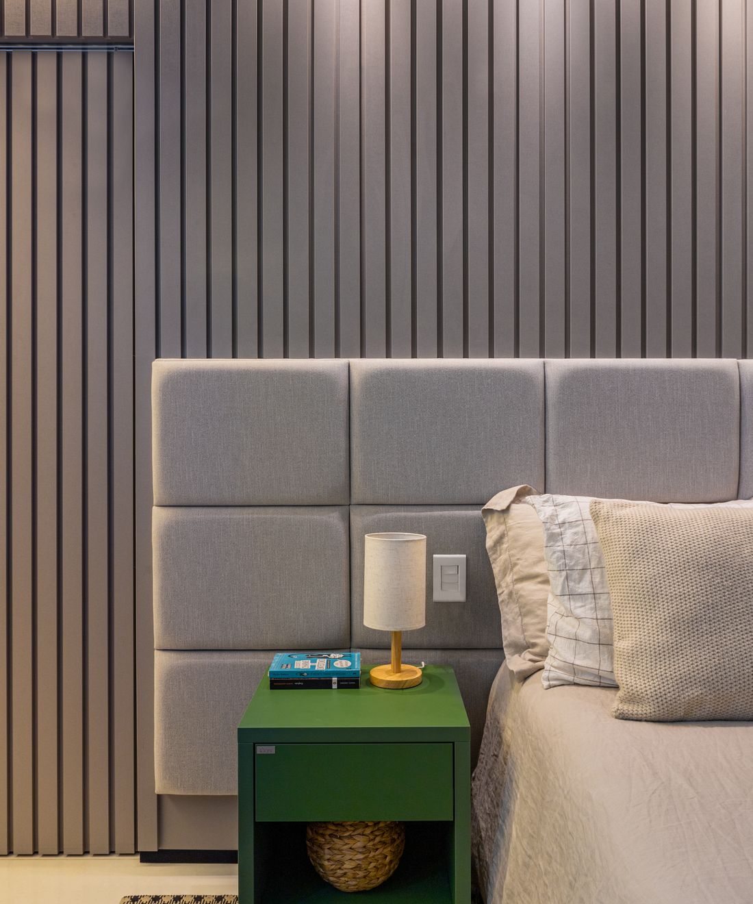 Quarto com cabeceira estofada em módulos, painel ripado chumbo e criado-mudo verde com abajur