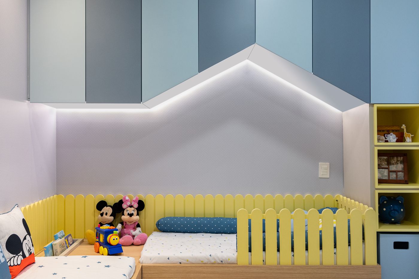 Quarto infantil com marcenaria azul em forma de casinha, faixa de LED, cama baixa com cerquinha amarela e nichos