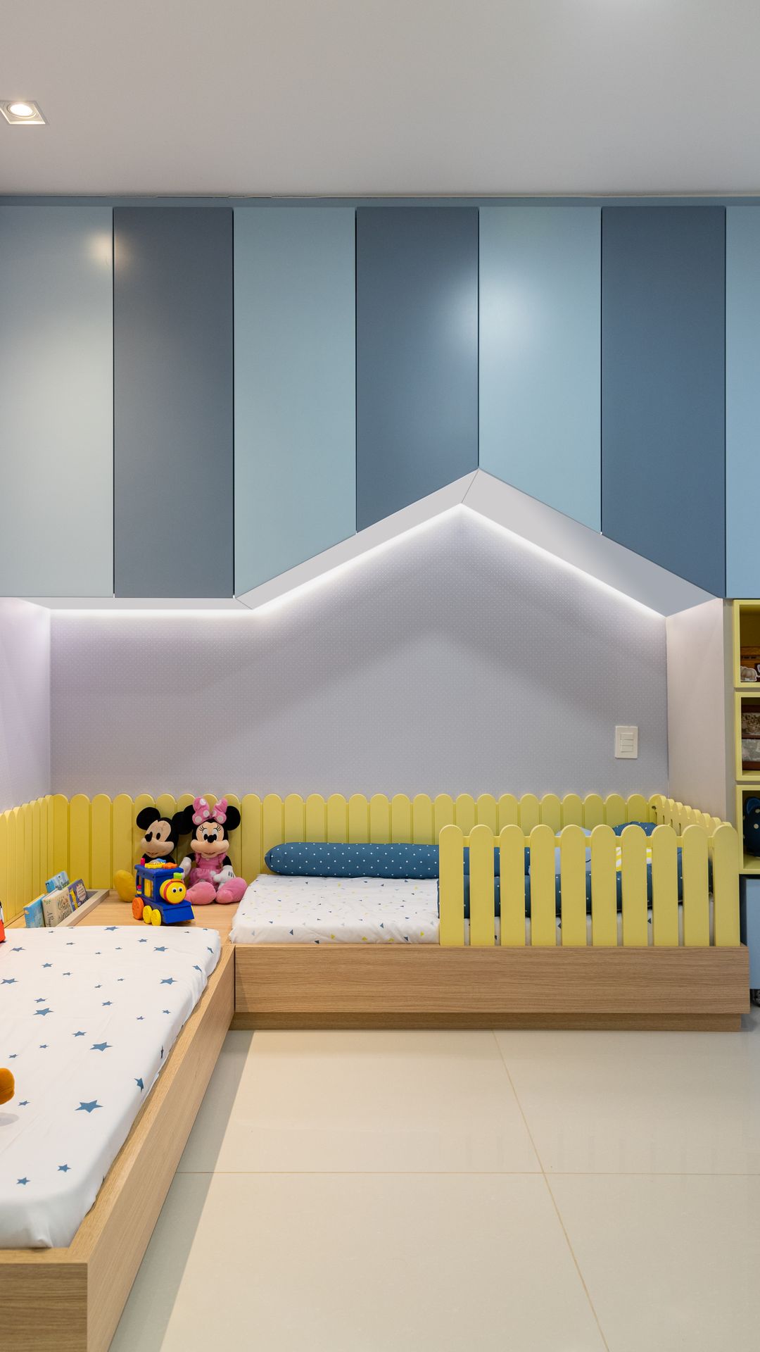 Quarto infantil com marcenaria azul em forma de casinha, faixa de LED e cama baixa com cerquinha amarela
