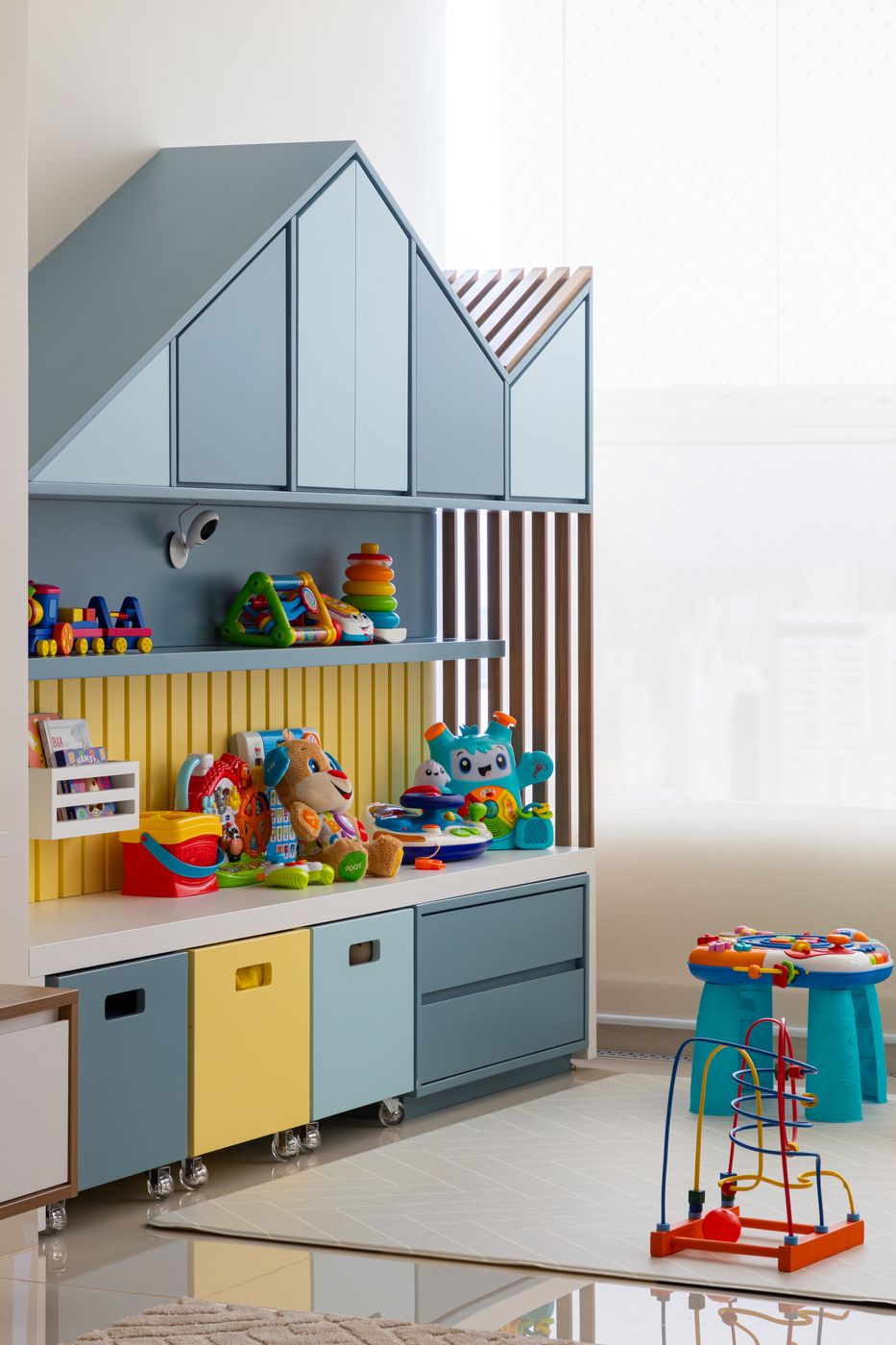 Brinquedoteca com casinha de madeira azul, prateleiras de brinquedos e mesa de atividades