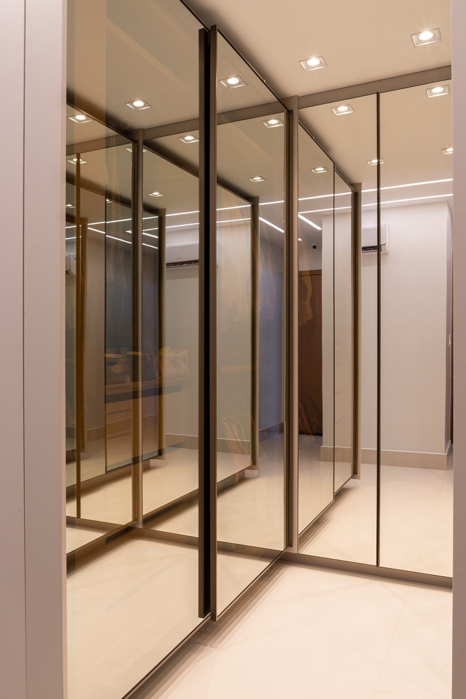 Closet com portas espelhadas bronze e perfis metálicos