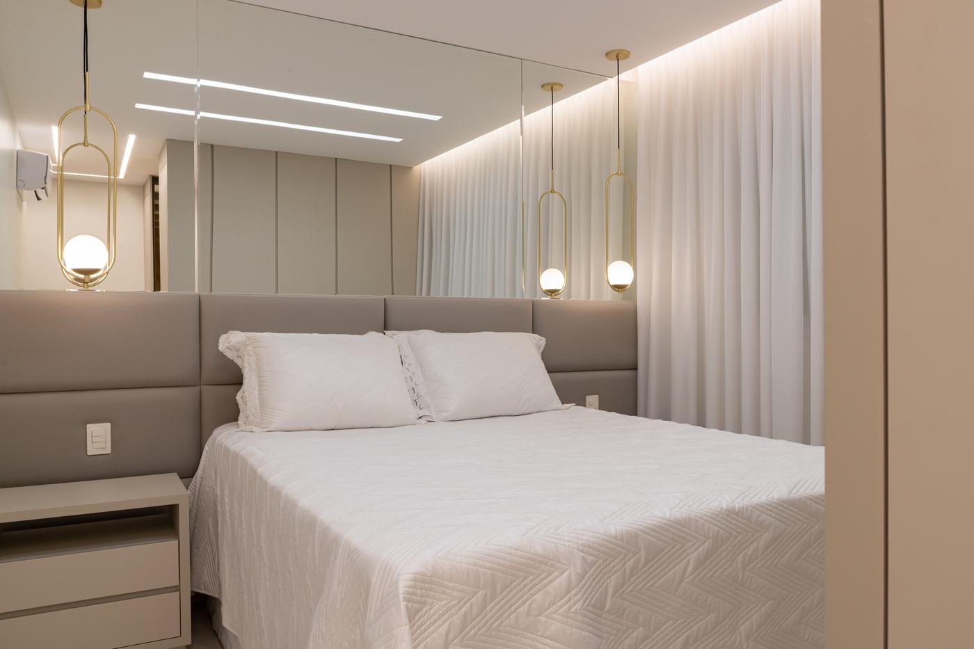 Quarto de casal com cabeceira estofada em módulos cinza, espelho e criado-mudo off-white