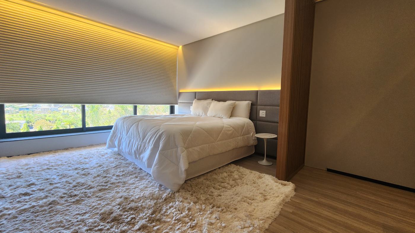 Quarto de casal com cabeceira em painéis estofados cinza com LED e divisória ripada de madeira