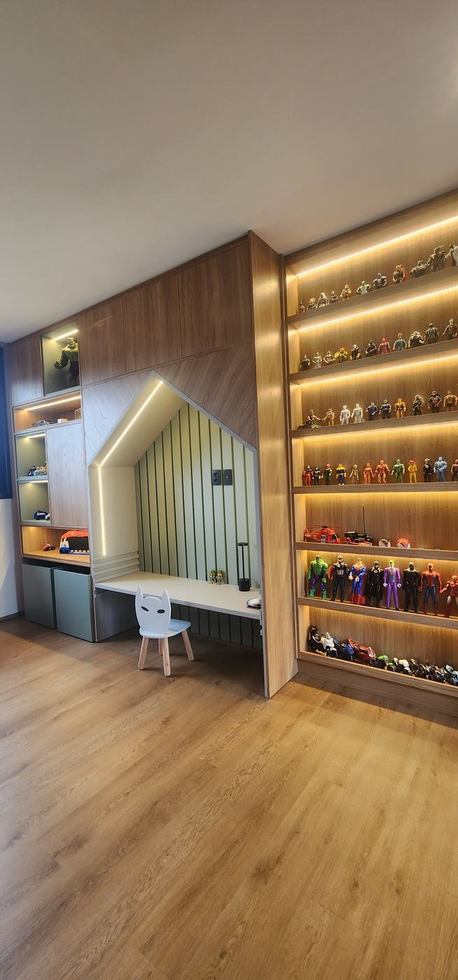 Quarto infantil com estante iluminada de brinquedos e escrivaninha em nicho de casinha, tudo em madeira clara