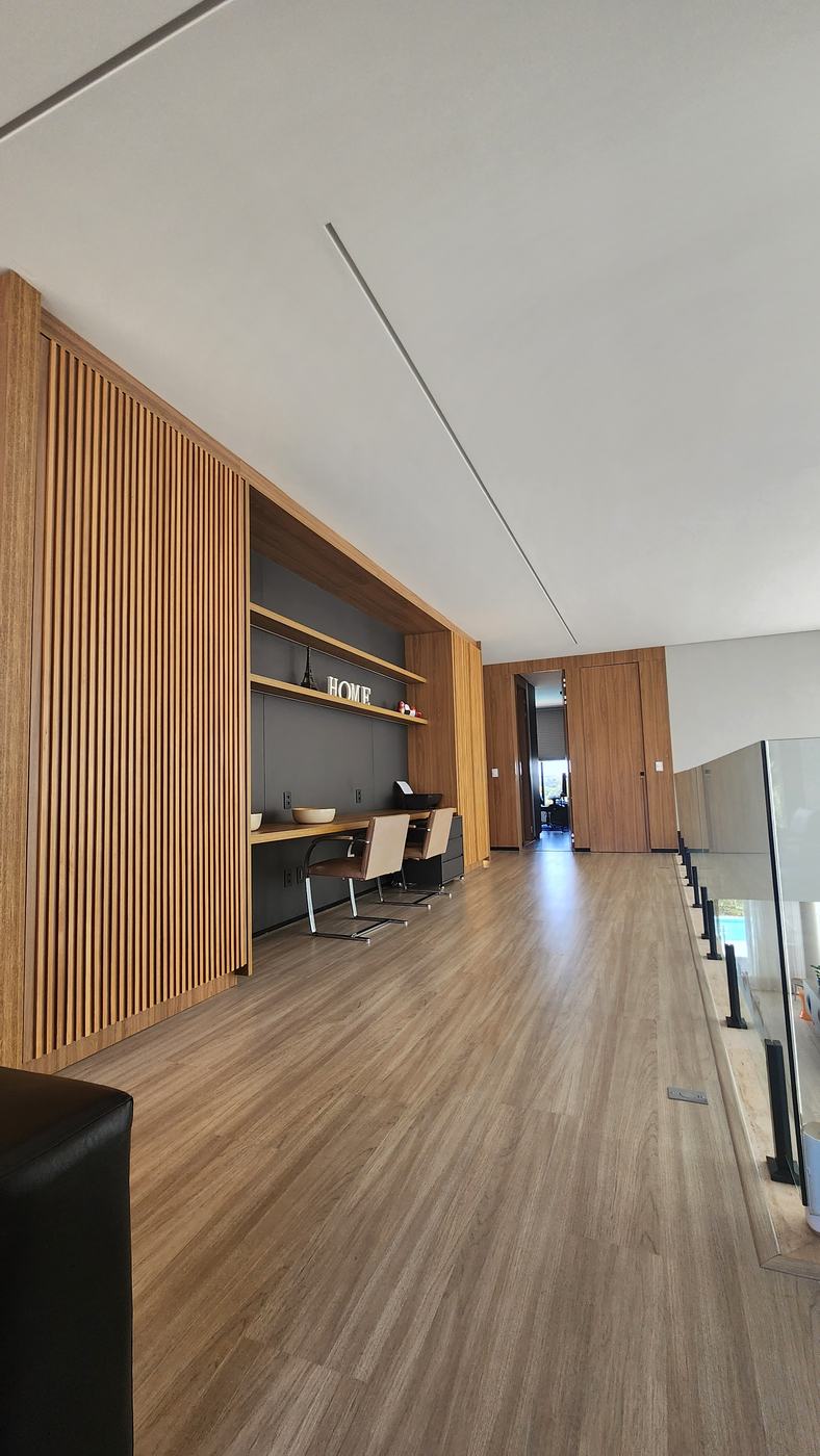 Home office no mezanino: bancada e prateleiras amadeiradas sobre fundo grafite, entre painel ripado e portas ocultas