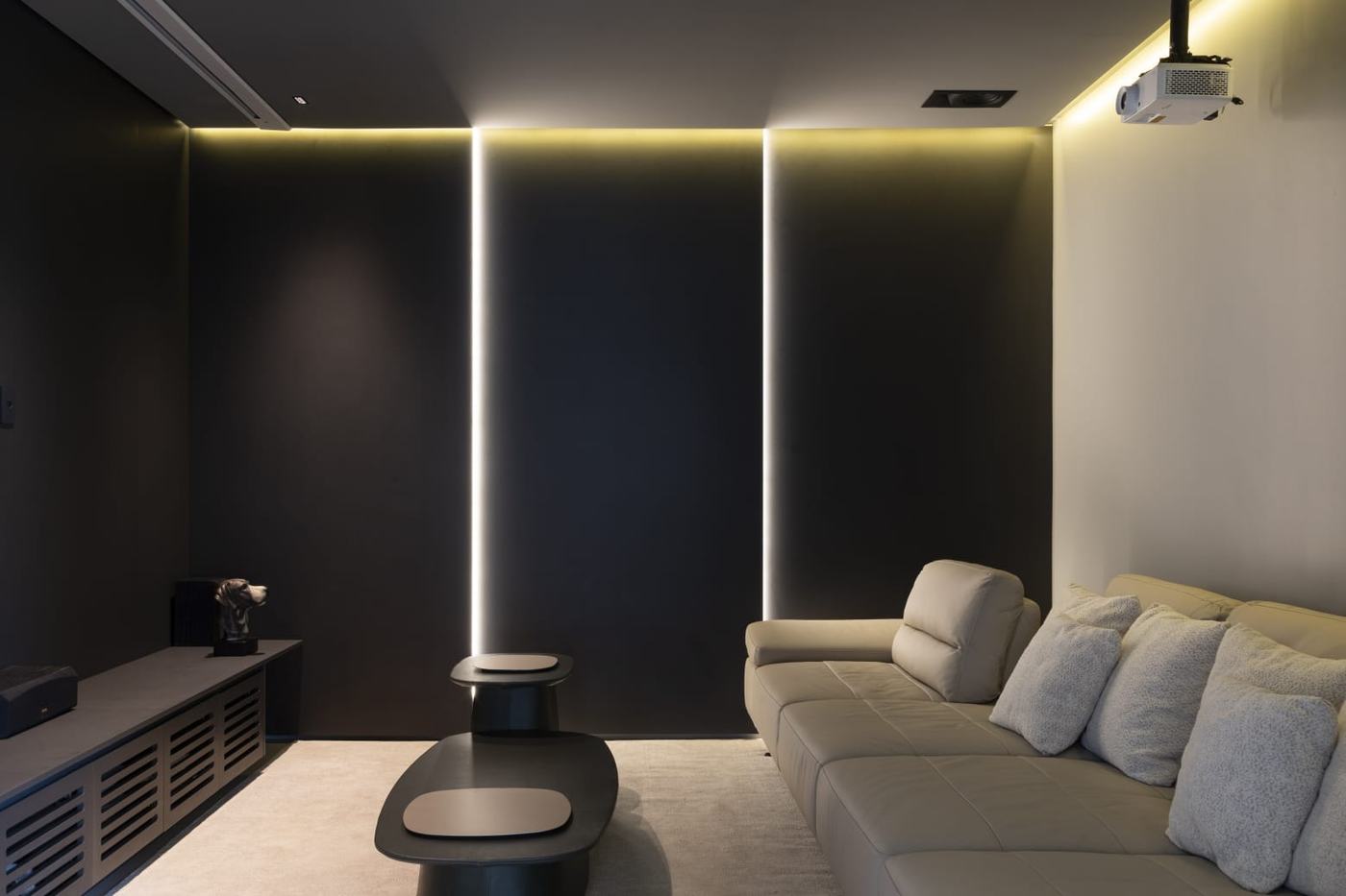 Sala de cinema com painéis pretos com frisos de LED, rack preto de portas venezianas e sofá claro