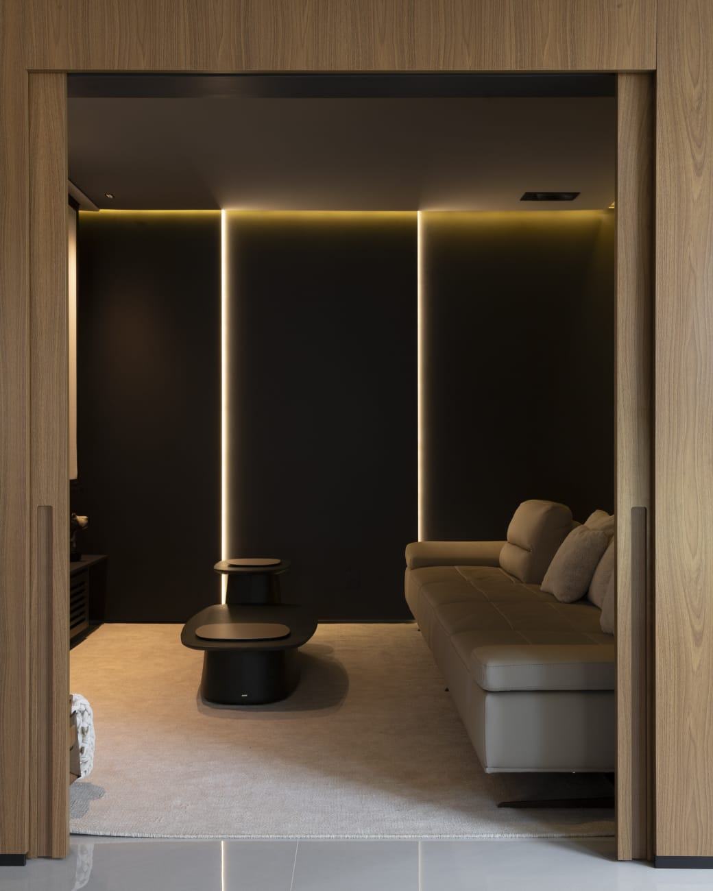 Portas de correr em madeira natural abrindo para a sala de cinema com painéis pretos e frisos de LED